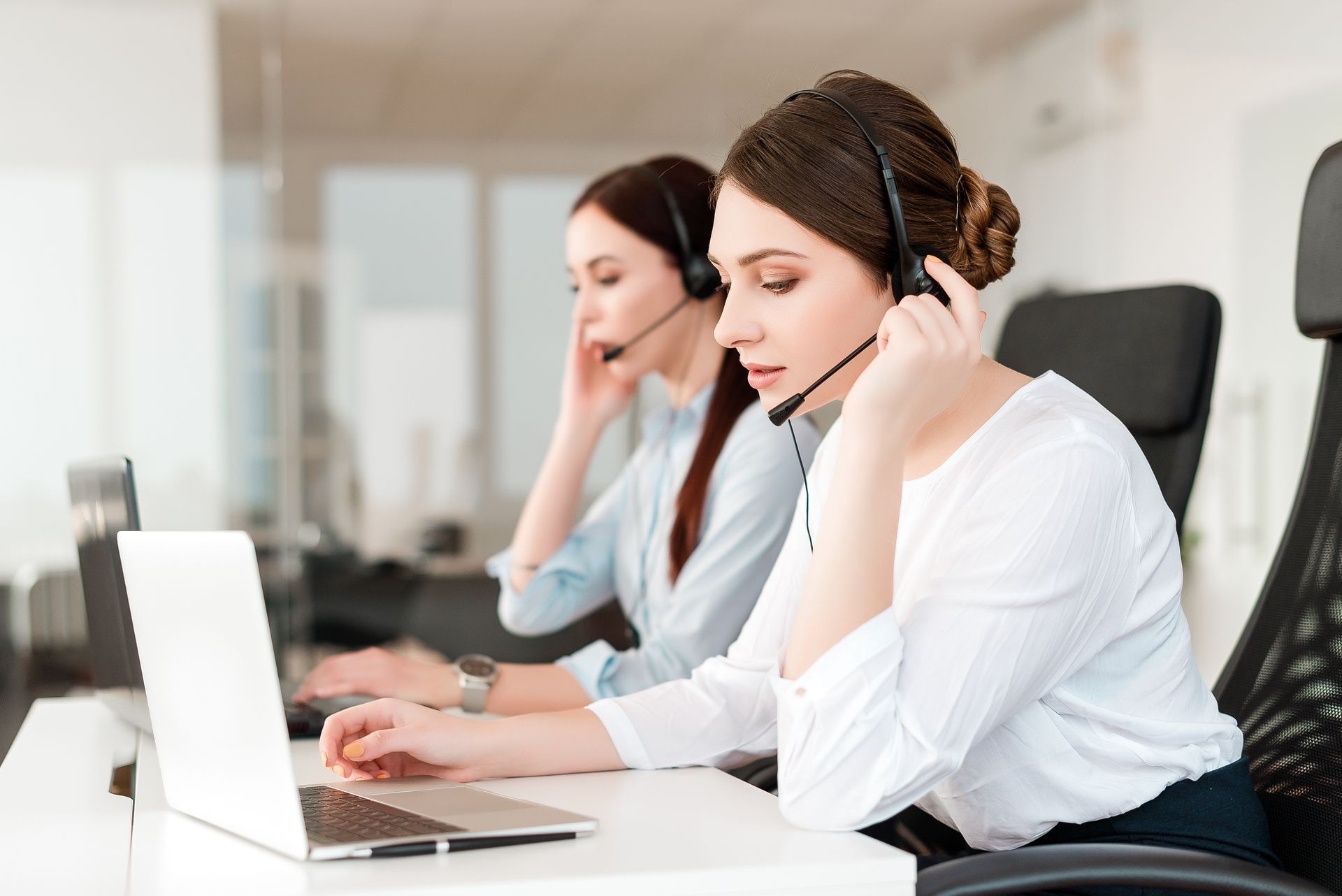 Friendly young female technical support dispatcher with a headset working in a call center on a hotline, talking on the phone. Portrait of an attractive customer care representative